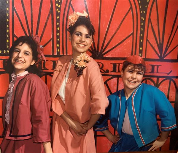 Three girls in costume posed in front of a red set.